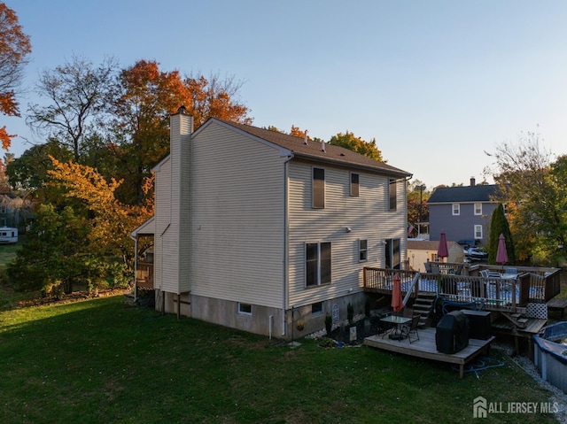 back of property with a chimney, a wooden deck, and a lawn