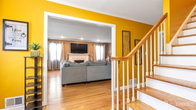 stairs featuring a fireplace, wood finished floors, visible vents, a healthy amount of sunlight, and crown molding