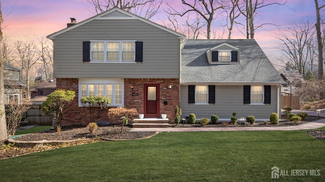 view of front of property with a yard, roof with shingles, fence, and brick siding