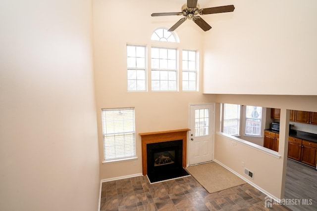 living area featuring visible vents, baseboards, a fireplace with flush hearth, a high ceiling, and a ceiling fan