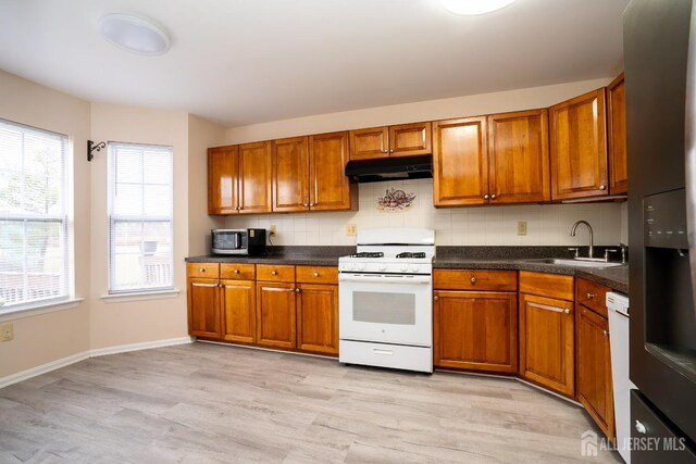 kitchen with sink, a wealth of natural light, white appliances, and light hardwood / wood-style flooring