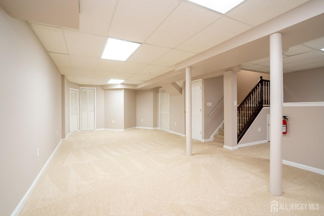 finished basement with stairs, light colored carpet, baseboards, and a drop ceiling