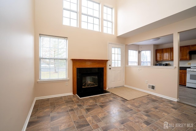 unfurnished living room featuring visible vents, baseboards, a towering ceiling, a glass covered fireplace, and stone finish floor