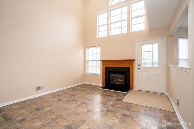 unfurnished living room featuring baseboards, visible vents, a towering ceiling, stone finish flooring, and a glass covered fireplace