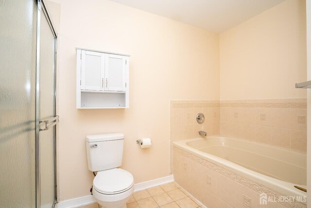 bathroom with a relaxing tiled tub, tile patterned floors, and toilet