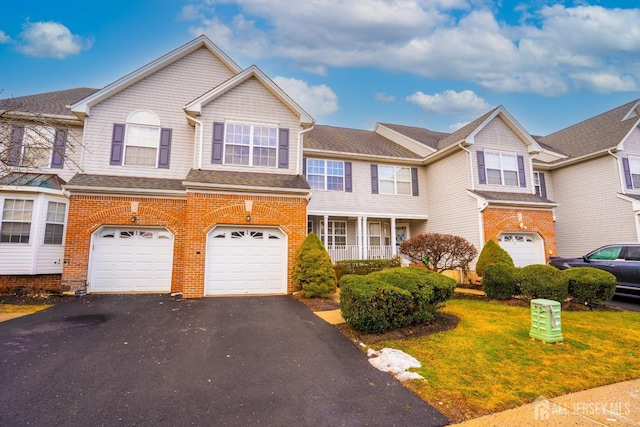 multi unit property with an attached garage, aphalt driveway, a front yard, and brick siding