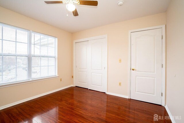 unfurnished bedroom featuring multiple windows, dark hardwood / wood-style flooring, and ceiling fan