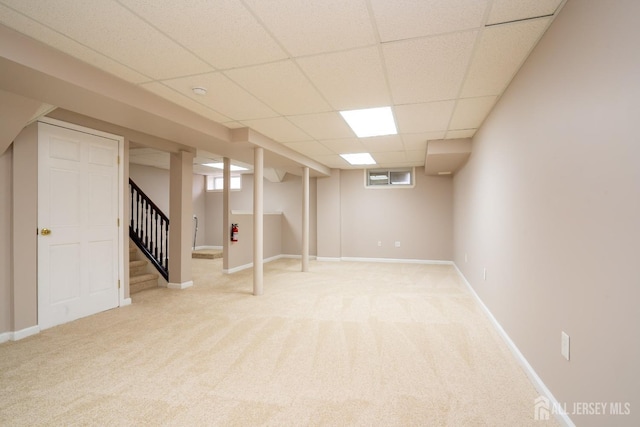 below grade area featuring light colored carpet, stairway, a paneled ceiling, and baseboards