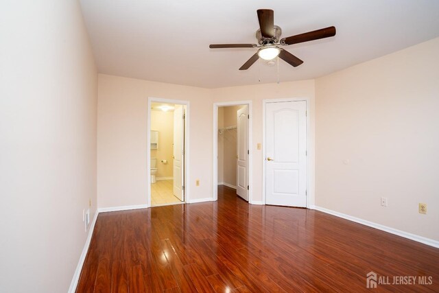 unfurnished bedroom with ensuite bath, a spacious closet, dark hardwood / wood-style floors, a closet, and ceiling fan