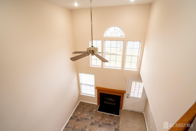 unfurnished living room featuring a high ceiling, a fireplace, baseboards, and ceiling fan