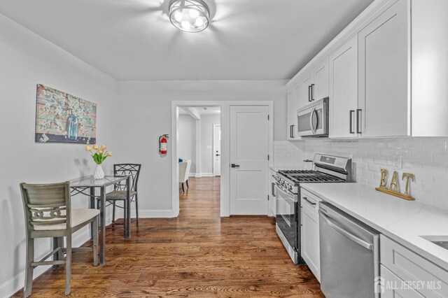 kitchen featuring appliances with stainless steel finishes, decorative backsplash, dark wood-type flooring, white cabinets, and light stone counters