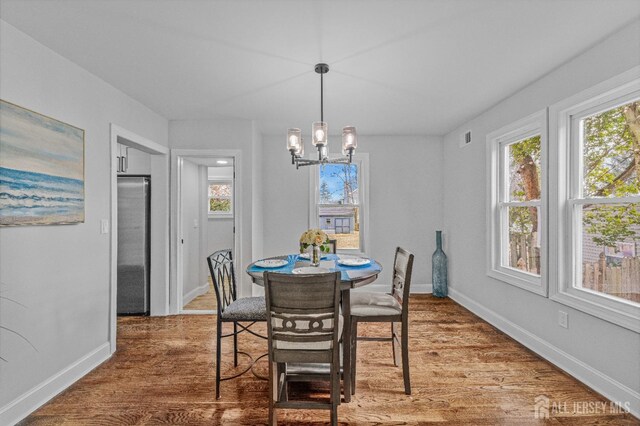 dining area featuring a healthy amount of sunlight, wood-type flooring, and a notable chandelier