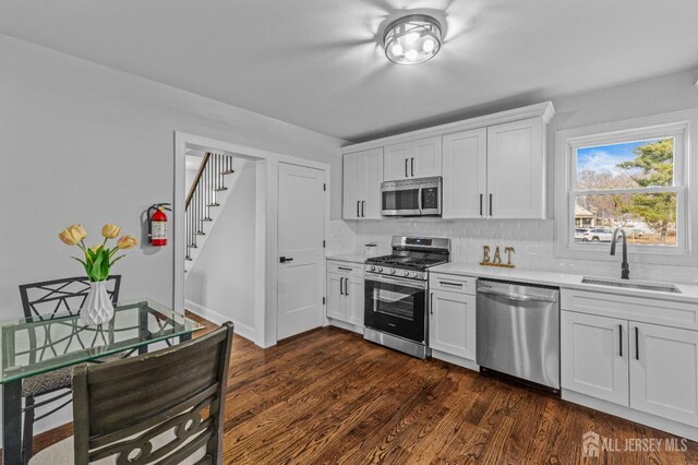 kitchen featuring appliances with stainless steel finishes, tasteful backsplash, dark wood-type flooring, white cabinets, and sink