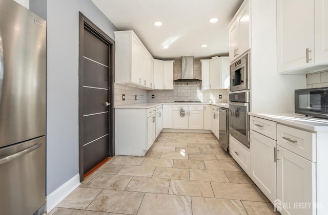 kitchen with decorative backsplash, light countertops, appliances with stainless steel finishes, white cabinetry, and wall chimney exhaust hood