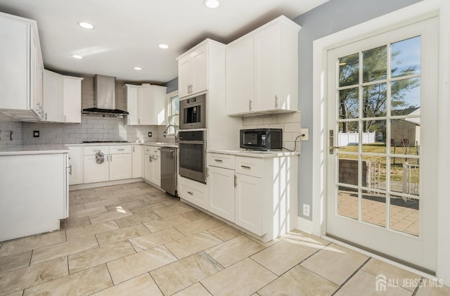 kitchen featuring decorative backsplash, light countertops, wall chimney range hood, and stainless steel appliances