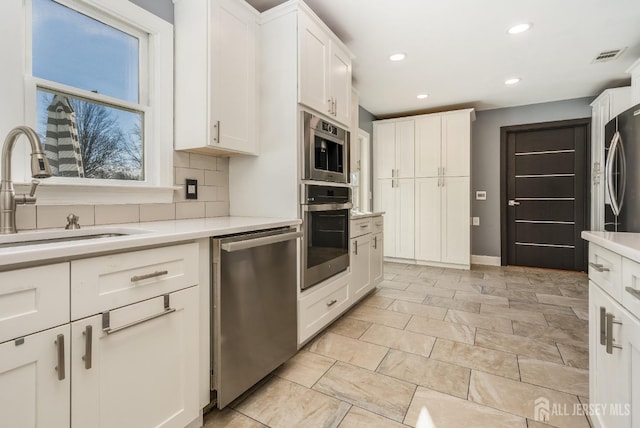 kitchen with a sink, light countertops, appliances with stainless steel finishes, white cabinetry, and tasteful backsplash