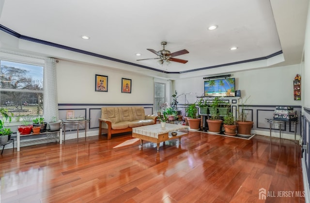 living area with a decorative wall, ornamental molding, a tray ceiling, and wood finished floors