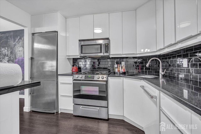 kitchen featuring dark wood finished floors, a sink, decorative backsplash, white cabinets, and appliances with stainless steel finishes