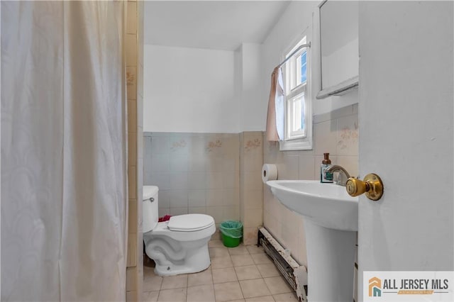 bathroom featuring tile patterned flooring, toilet, baseboard heating, wainscoting, and tile walls