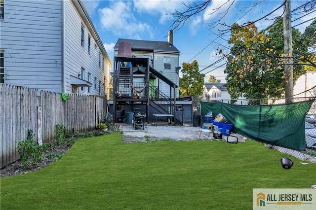 back of house with stairs, a patio area, a fenced backyard, and a lawn