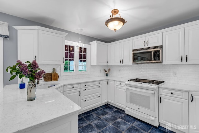 kitchen featuring white gas stove, white cabinetry, hanging light fixtures, light stone countertops, and backsplash