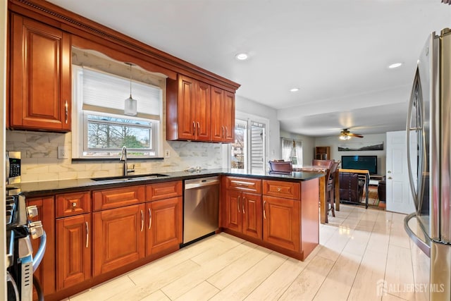 kitchen featuring tasteful backsplash, appliances with stainless steel finishes, a peninsula, a ceiling fan, and a sink