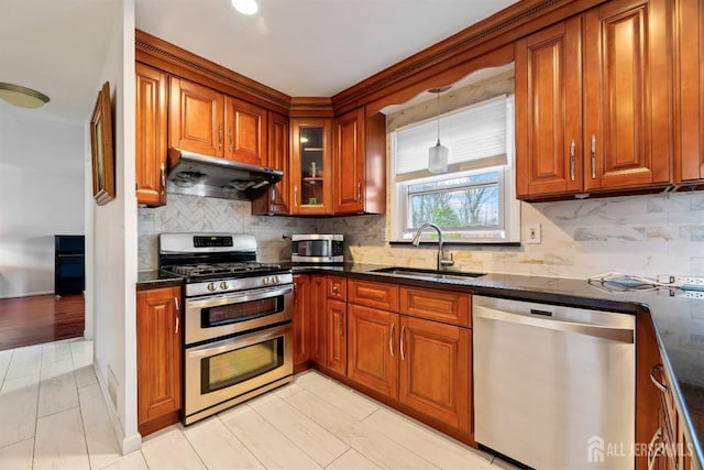 kitchen with a sink, brown cabinets, appliances with stainless steel finishes, and under cabinet range hood