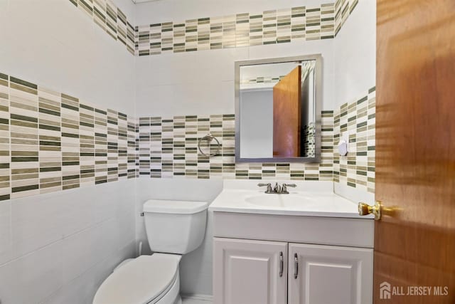 bathroom featuring tasteful backsplash, toilet, vanity, and tile walls