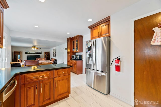 kitchen with a ceiling fan, a peninsula, appliances with stainless steel finishes, dark countertops, and brown cabinets