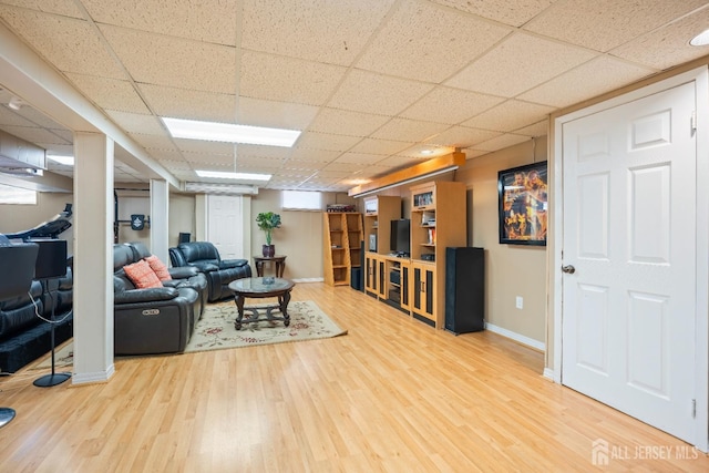 living area featuring a drop ceiling, baseboards, and wood finished floors