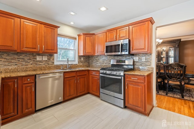 kitchen with appliances with stainless steel finishes, a sink, backsplash, and light stone countertops