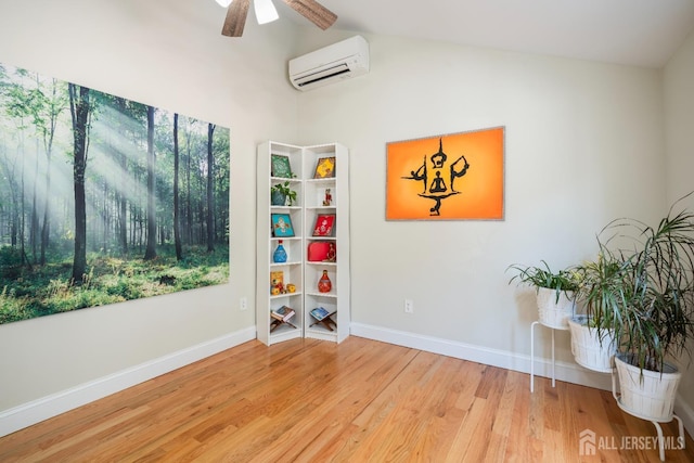 empty room featuring baseboards, a ceiling fan, lofted ceiling, wood finished floors, and a wall mounted air conditioner