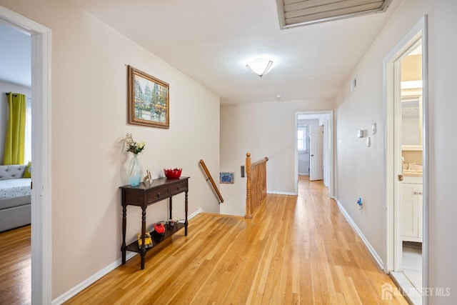 corridor with baseboards, visible vents, light wood finished floors, and an upstairs landing