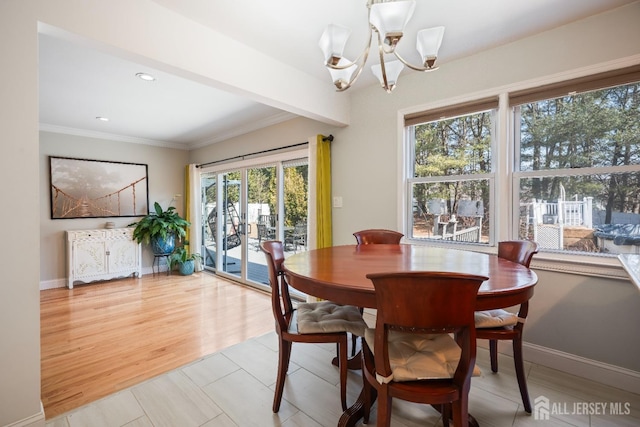 dining area with baseboards, ornamental molding, light wood-type flooring, and an inviting chandelier