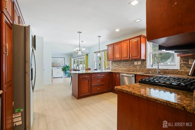 kitchen with dark stone counters, appliances with stainless steel finishes, a peninsula, pendant lighting, and backsplash