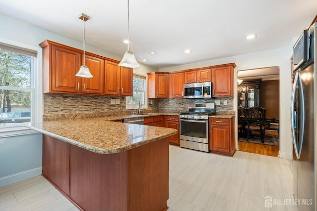 kitchen with hanging light fixtures, decorative backsplash, appliances with stainless steel finishes, a sink, and a peninsula