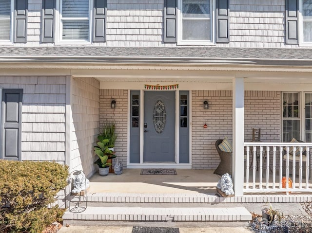 property entrance featuring brick siding, a porch, and roof with shingles