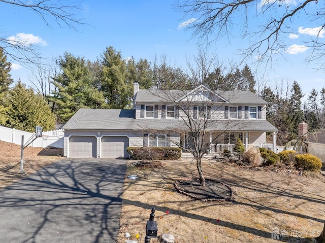 view of front of property featuring a porch, aphalt driveway, an attached garage, fence, and a chimney