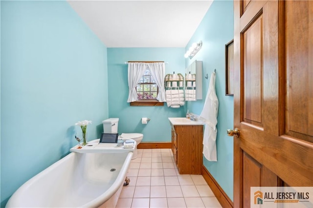 bathroom featuring a soaking tub, vanity, toilet, tile patterned floors, and baseboards