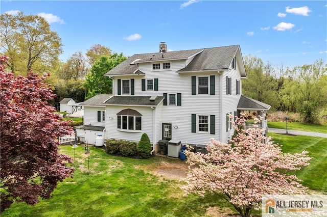 rear view of property with a lawn, a chimney, and roof with shingles