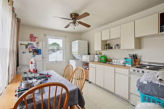 kitchen with white appliances, stacked washer / drying machine, ceiling fan, and light countertops