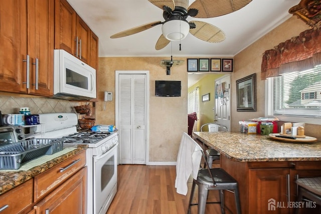 kitchen featuring white appliances, light wood finished floors, brown cabinetry, decorative backsplash, and ceiling fan
