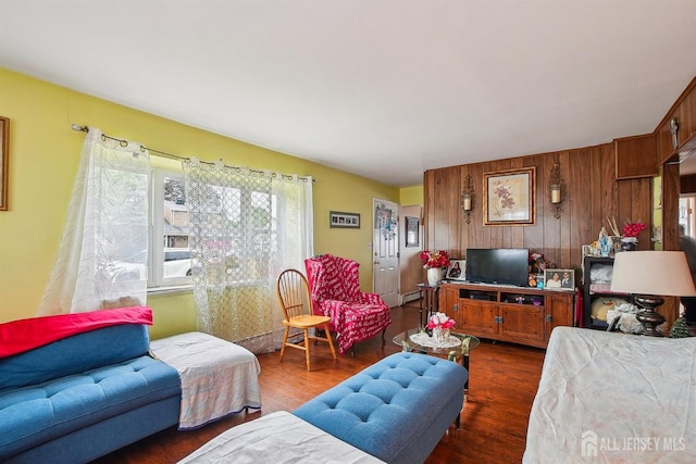 living area featuring dark wood-style floors, wooden walls, and a baseboard radiator