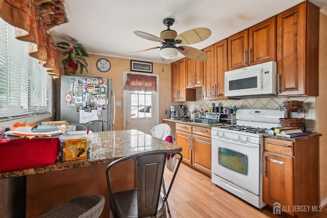 kitchen with white appliances, light wood-type flooring, brown cabinets, and decorative backsplash