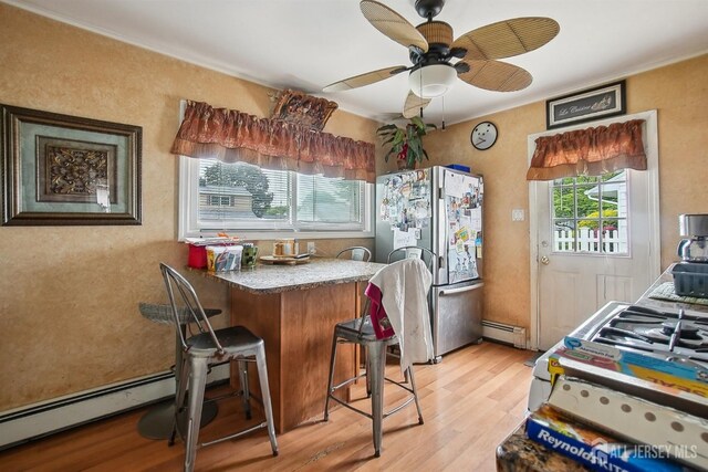 kitchen with freestanding refrigerator, baseboard heating, light wood-type flooring, and a breakfast bar