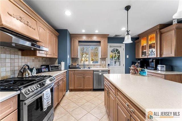 kitchen with light tile patterned flooring, a sink, stainless steel appliances, light countertops, and decorative light fixtures