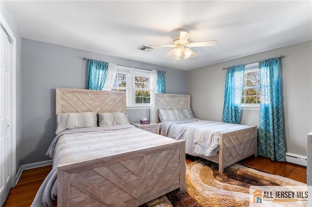 bedroom with wood finished floors, a closet, baseboard heating, and baseboards