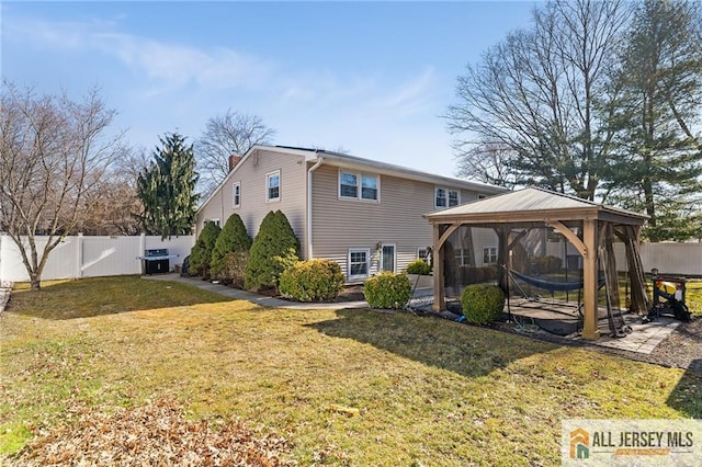 back of house featuring a fenced backyard, a chimney, a gazebo, a patio area, and a lawn