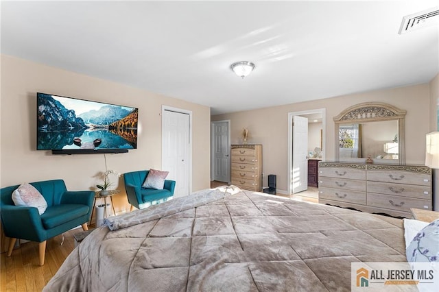 bedroom with visible vents, ensuite bath, a closet, and wood finished floors