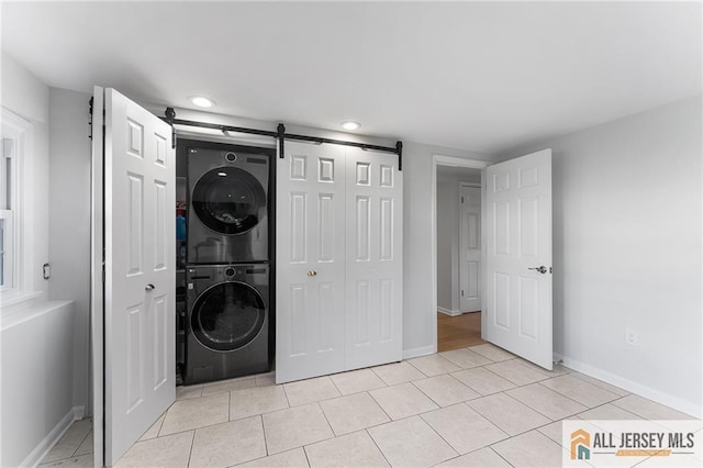 clothes washing area featuring light tile patterned flooring, laundry area, stacked washer / drying machine, and a barn door